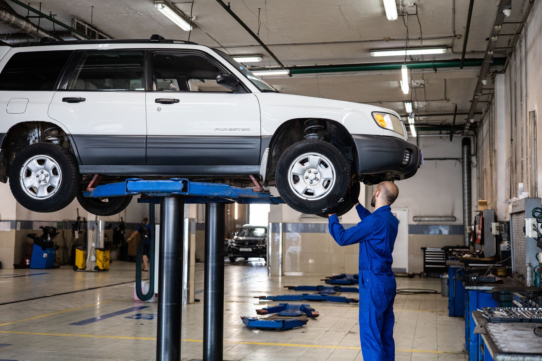 A mechanic inspecting a vehicle raised on a workshop lift.
